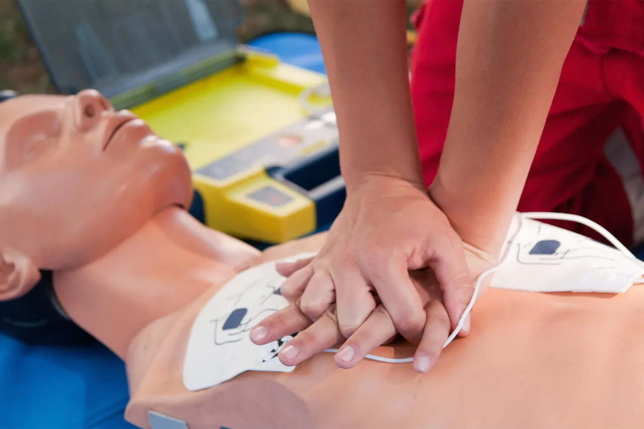 Person providing CPR to a dummy with a defibrillator